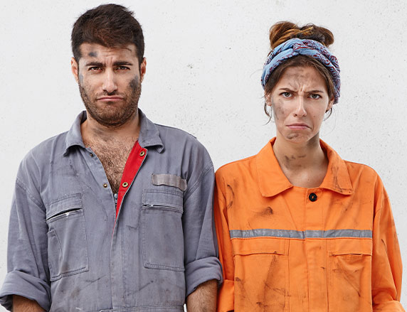 Ein Mann und eine Frau beide mit eher traurig-grimmigen Gesichtsausdruck, deren Arbeitskleidung sowie ihre Gescichter schwarz verdreckt sind und frontal in die Kamera blicken